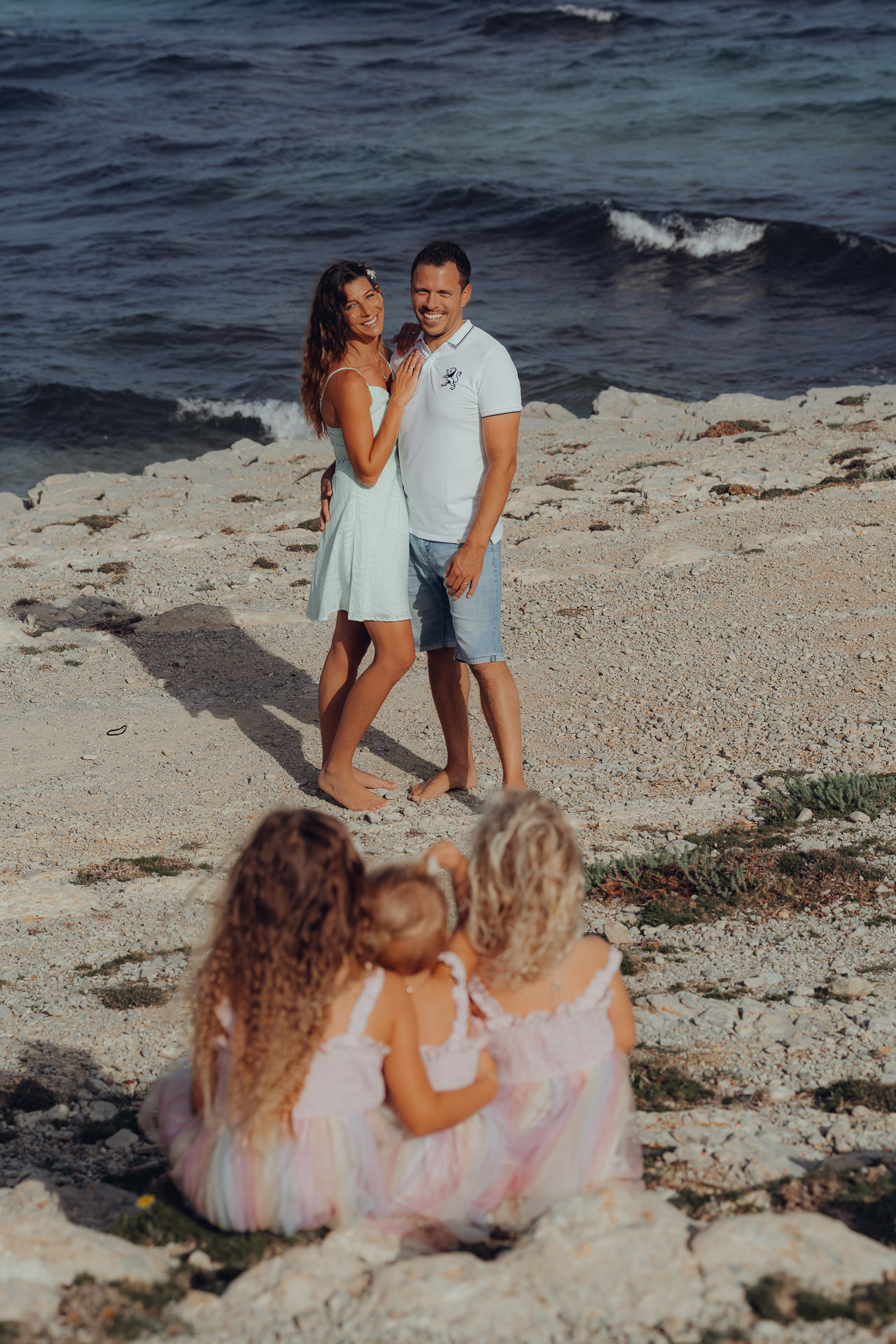 Drei kleine Mädchen schauen sitzend zu den glücklichen Eltern