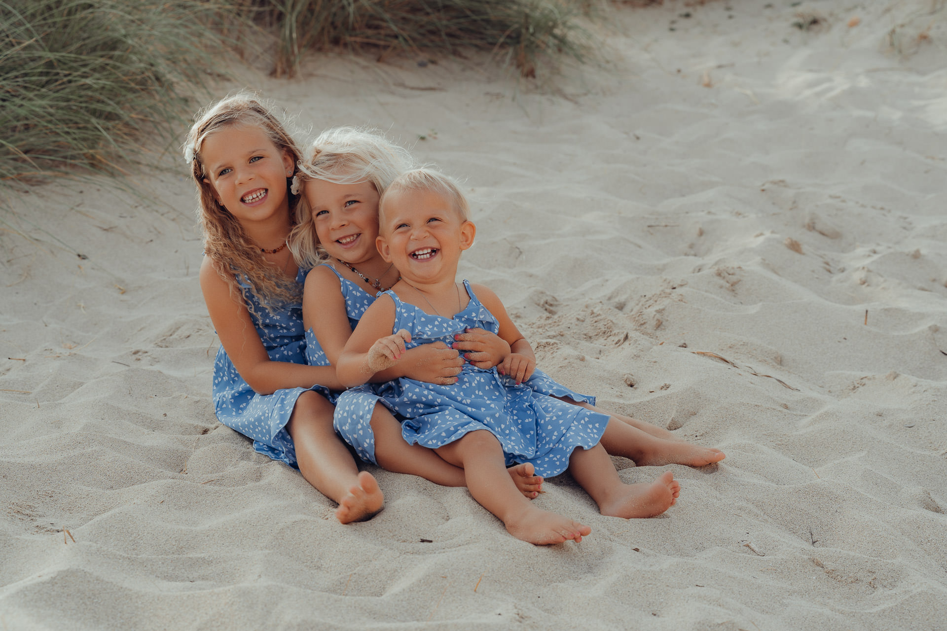 Drei kleine Mädchen sitzen im Sand und lächeln für ein Fotoshooting