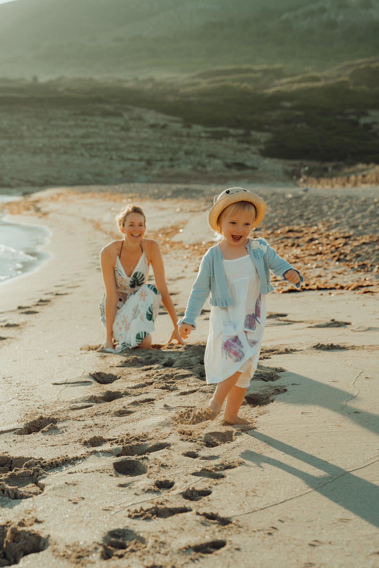 Ein kleines Mädchen läuft lachend bei Sonnenuntergang am Strand von der Mutter weg.