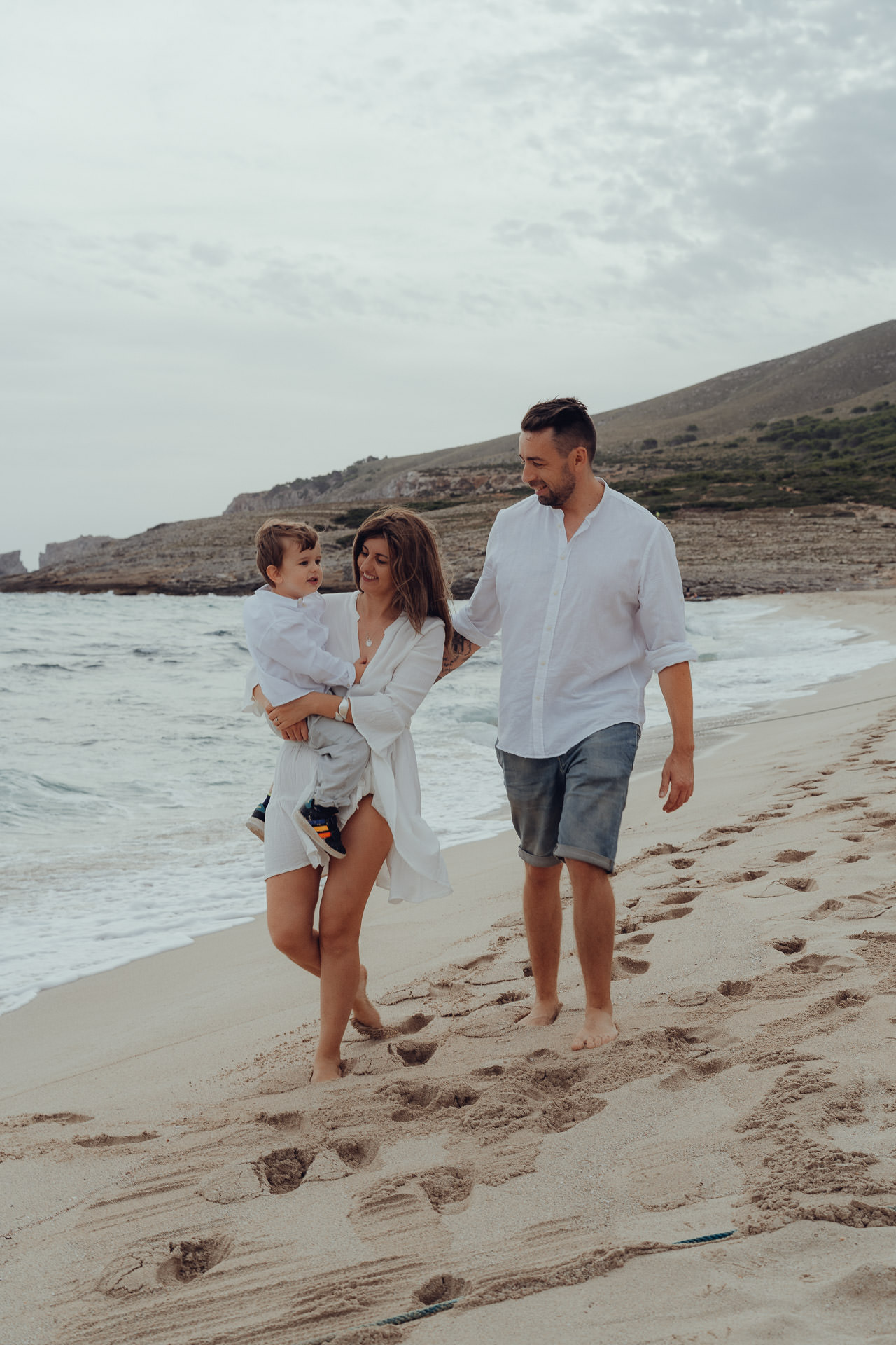 Glückliche Familie läuft am Strand der Cala Mesquida mit einem Jungen auf dem Arm.
