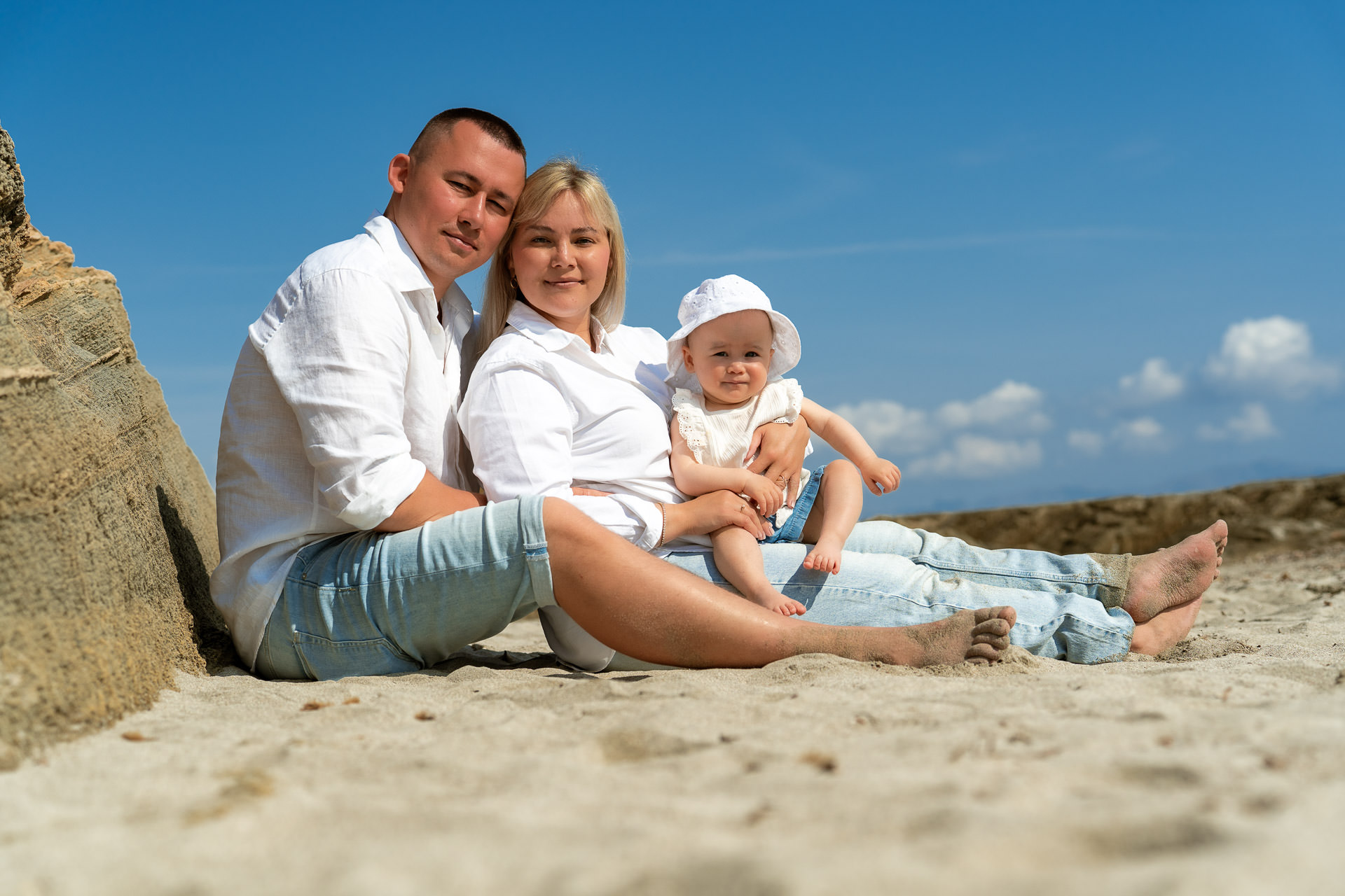Junge Familie sitzt mit kleinem Baby im Sand am Strand von Can Picafort