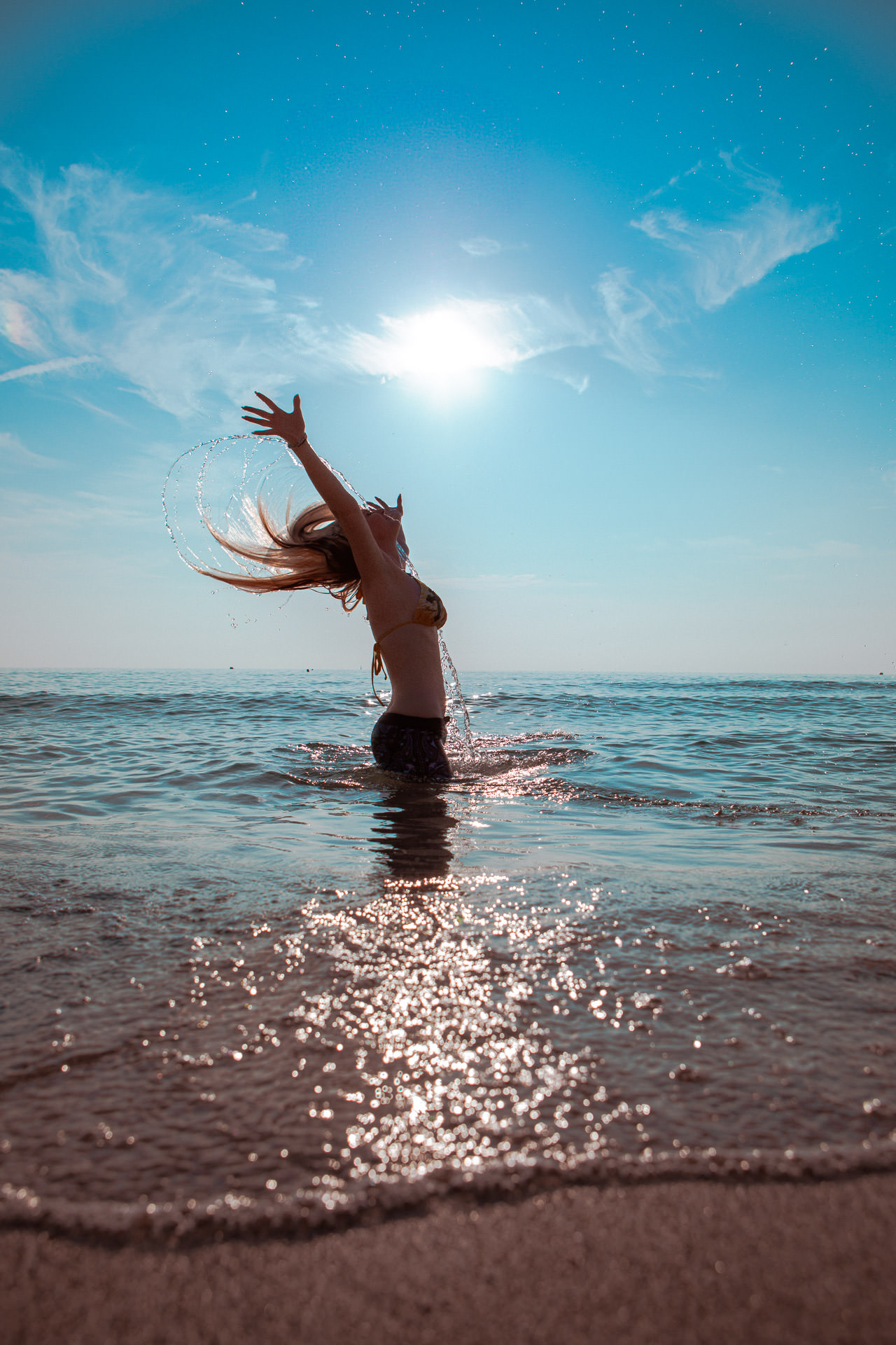 Ein Model sitzt im Wasser und schleudert ihre nassen Haare aus dem Meer